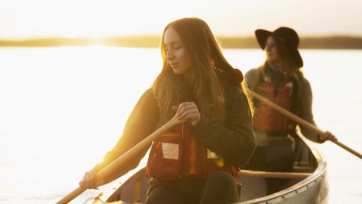 Kaksi henkilö meloo järvellä auringonlaskun aikaan