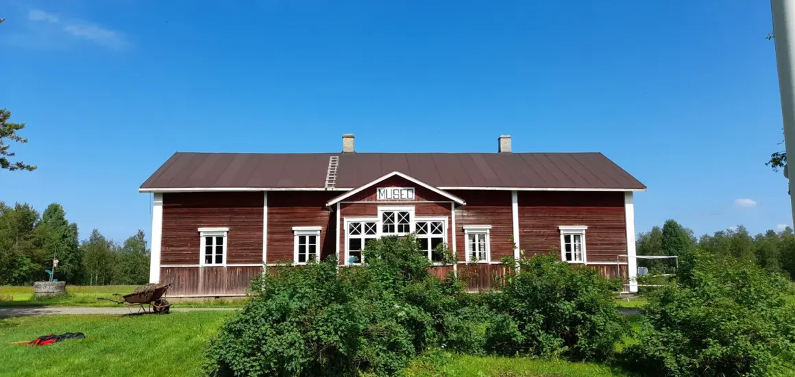 Kuvassa punainen museorakennus vihreän luonnon keskellä, taivas on sininen.