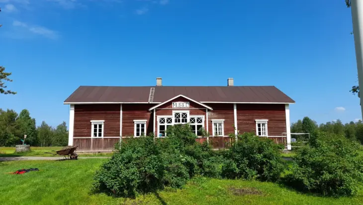 Kuvassa punainen museorakennus vihreän luonnon keskellä, taivas on sininen.