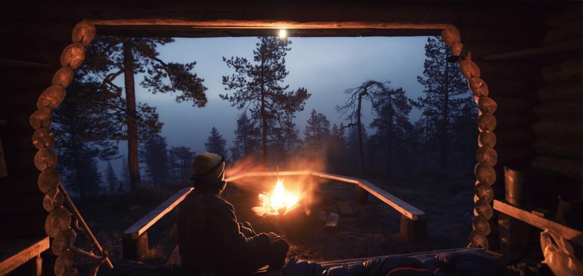 henkilö nuotiolla, hämärä metsämaisema